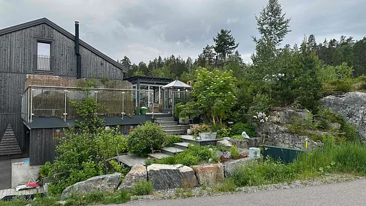 Grått hus med skorstein uten på hus, og pent opparbeid hage